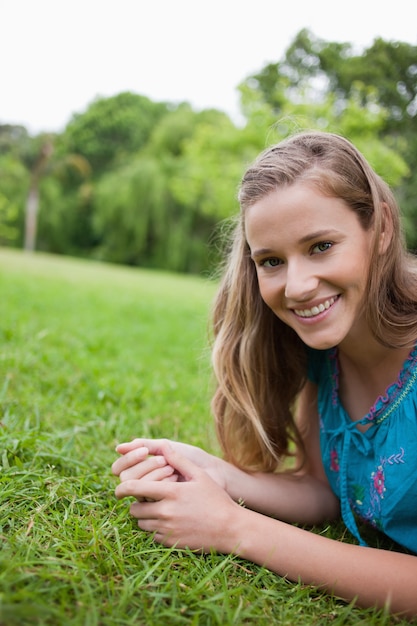 Junge lächelnde Frau, die auf dem Gras in einem allgemeinen Garten liegt