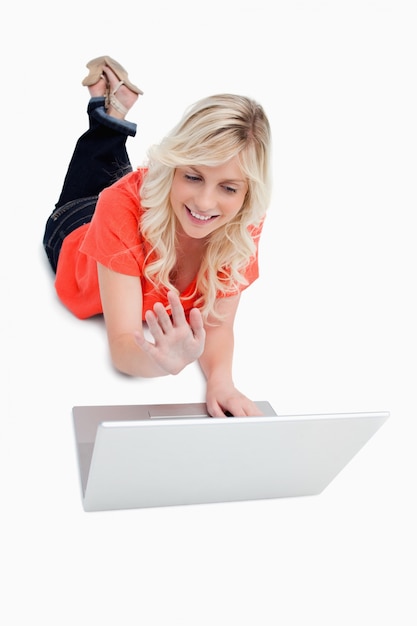 Junge lächelnde Frau, die ihre Beine beim Wellenartig bewegen ihrer Hand vor ihrem Laptop kreuzt