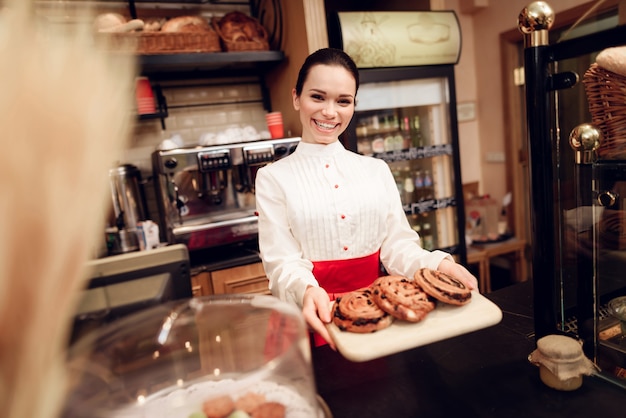 Junge lächelnde Frau, die mit Rolls in der Bäckerei steht