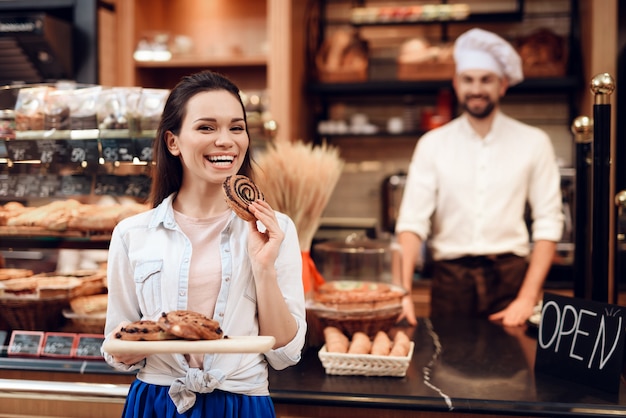 Junge lächelnde Frau, die Rolls in der modernen Bäckerei isst