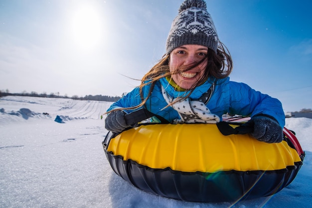 Junge lächelnde Frau hält sich für Schlitten-Schneeschläuche im Winter fest