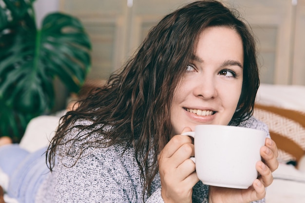 Junge lächelnde Frau im grauen Lügen auf dem Bett mit weißer Schale.