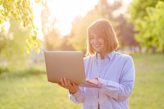 Junge lächelnde Frau im grünen Park mit Laptop