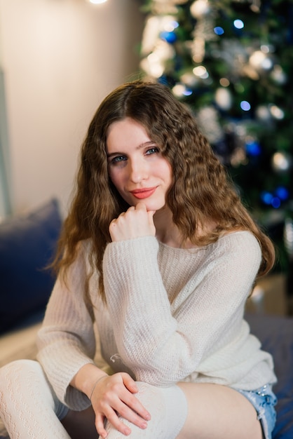Junge lächelnde Frau in einer Strickjacke, Winterferien in verziertem Hauptinnenraum mit Weihnachtsbaum.