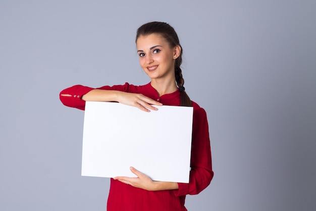 Junge lächelnde Frau in roter Bluse mit weißem Blatt Papier auf grauem Hintergrund im Studio