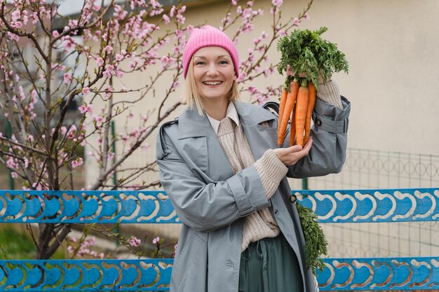 Junge lächelnde Frau mit einem Strauß frischer Bio-Karotten im Garten draußen Menschen kaufen bewusst regionale Produkte vom lokalen Markt ein, nachhaltige Lebensmittel, keine Plastikverpackungen