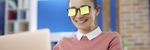 Junge lächelnde Frau mit gelben Stickars auf Brille mit Fragezeichen funktioniert auf Laptop