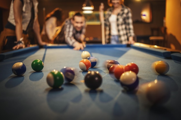 Foto junge, lächelnde, fröhliche freunde spielen nach der arbeit billard in der bar. sie engagieren sich in der freizeitgestaltung. selektiver fokus, fokus auf billardkugeln.