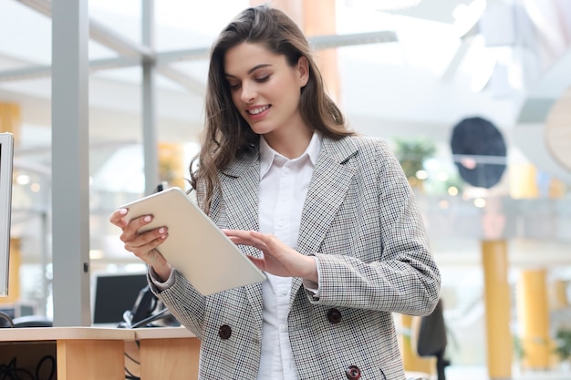 Junge lächelnde Geschäftsfrau im Büro, das an digitaler Tablette arbeitet.