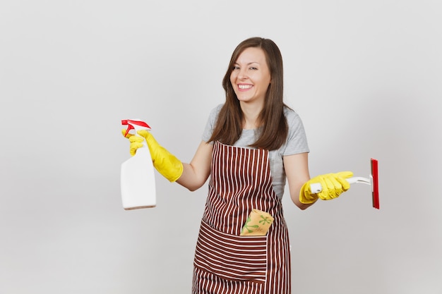 Junge lächelnde Hausfrau in gelben Handschuhen, gestreifte Schürze, Putzlappen in der Tasche isoliert auf weißem Hintergrund. Haushälterin Frau mit Rakel, Sprühflasche mit sauberer Flüssigkeit. Flaschenkopierraum.