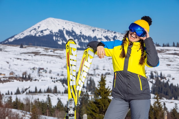 Junge lächelnde hübsche Frau, die Ski hält. Berge im Hintergrund. Winterreisen. Platz kopieren