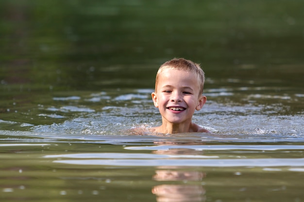 Junge lächelnde Kinderjungenschwimmen im schlammigen Wasser