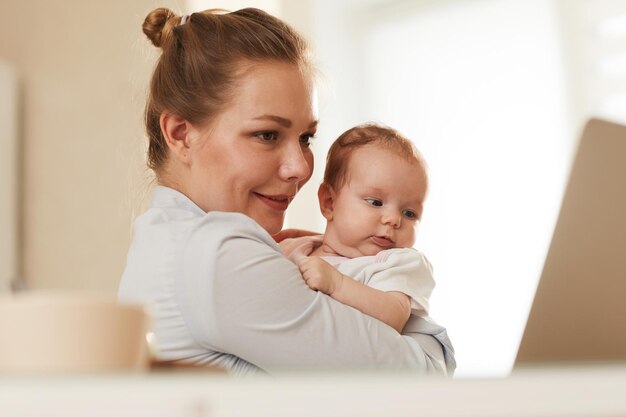 Junge lächelnde Mutter, die ihr Baby der Großmutter zeigt, die sie über Skype anruft