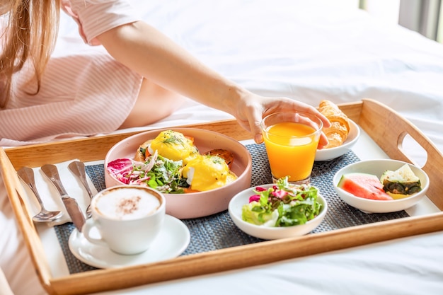 Junge lächelnde schöne Frau, die Frühstück im Bett im gemütlichen Hotelzimmer hat