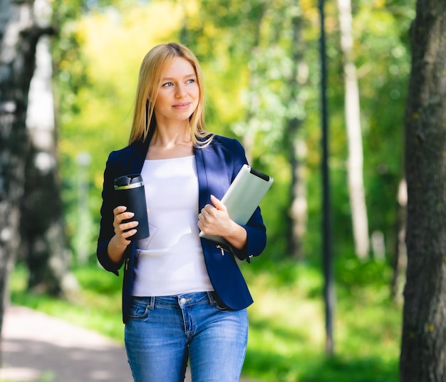 Junge lächelnde schöne Frau im Park mit Tablet-Gadget und drahtlosen Kopfhörern, die Fernarbeit mit grünem Energiekonzept genießen