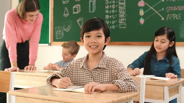 Junge lächelt in die Kamera, während ein Schüler eine Antwort auf seinem Antwortblatt schreibt Pädagogik