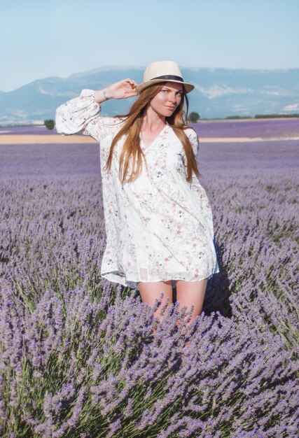 Junge, langhaarige Frau mit Hut und Kleid unter Lavendelfeldern in der Provence, Frankreich