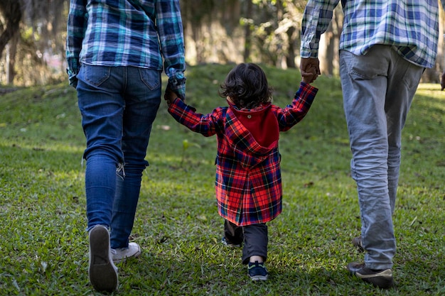 Junge lateinamerikanische Familie, die zusammen Hand in Hand geht und den Nachmittag im Park genießt Familienkonzept