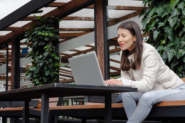 Junge lateinamerikanische Frau, die draußen an einem Tisch sitzt, während sie ihren Laptop benutzt