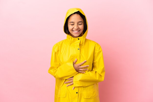 Junge lateinamerikanische Frau, die einen regendichten Mantel über isoliertem Hintergrund trägt und viel lächelt