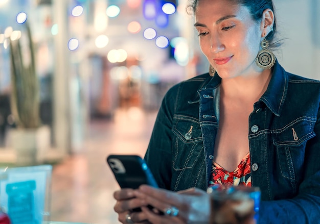 Junge lateinamerikanische Frau, die sich in einem Restaurant oder Pub ein mobiles Gerät ansieht