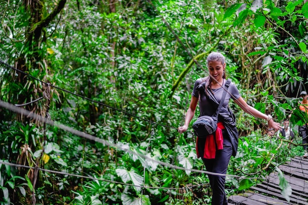 Junge lateinamerikanische Frau im Dschungel, die eine ökologische Wanderung der Hängebrücke in Kolumbien überquert