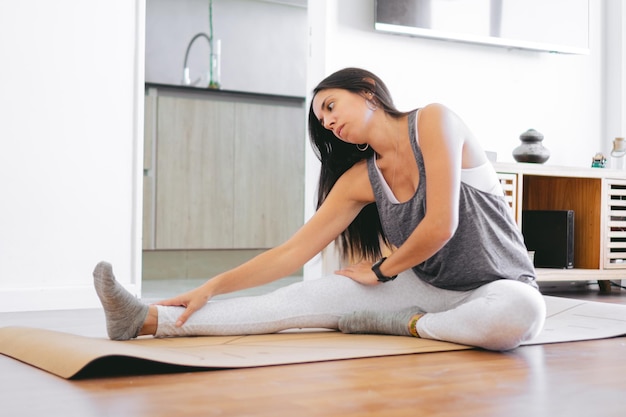 Junge lateinamerikanische Frau in ihrem Wohnzimmer dehnt sich auf einer Yogamatte. Kopierraum