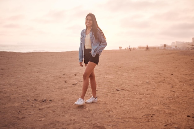 Junge lateinamerikanische Frau posiert während eines wunderschönen Sonnenuntergangs auf dem Sand