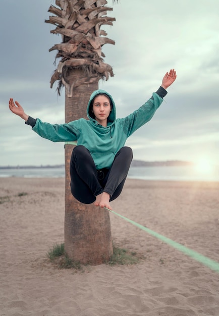 Junge lateinamerikanische Frau sitzt und balanciert auf dem Gurtband, das Yoga am Strand von La Serena auskleidet