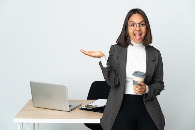 Junge lateinamerikanische Geschäftsfrau, die in einem Büro arbeitet, isoliert auf weißem Hintergrund mit schockiertem Gesichtsausdruck