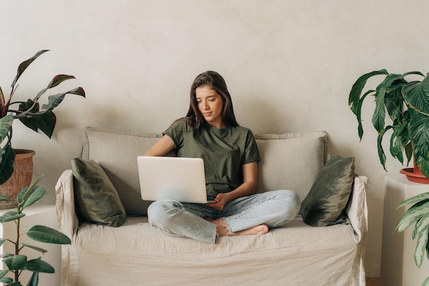 Junge lateinamerikanische Studentin sitzt auf dem Sofa und benutzt einen Laptop zum Online-Lernen