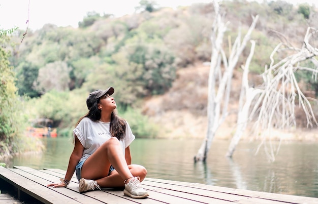 Junge lateinische Frau, die auf dem Pier des Sees sitzt und die Natur genießt