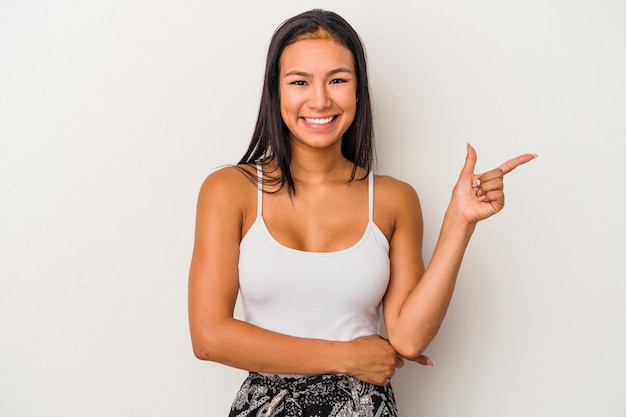 Junge lateinische Frau, die auf weißem Hintergrund lokalisiert wird, lächelt fröhlich und zeigt mit dem Zeigefinger weg.