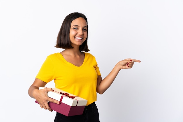 Junge lateinische Frau, die ein Geschenk lokalisiert auf weißem Zeigefinger zur Seite hält und ein Produkt präsentiert