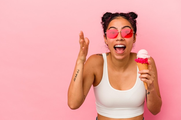 Junge lateinische Frau, die eine Eiscreme lokalisiert auf rosa Hintergrund hält, die eine angenehme Überraschung empfängt, aufgeregt und Hände erhebt.