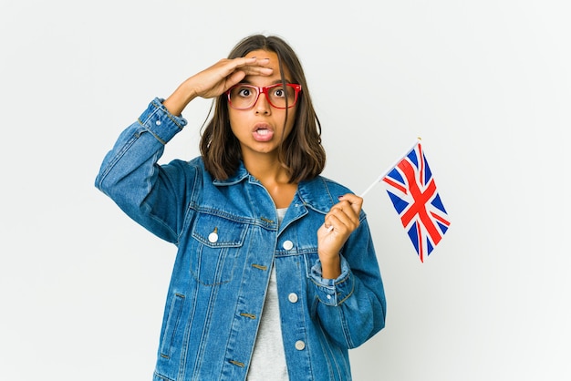 Junge lateinische Frau, die eine englische Flagge hält, die weit weg schaut und Hand auf Stirn hält.