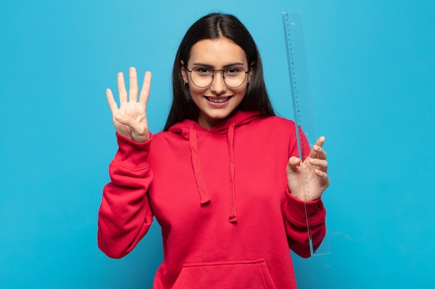 Junge lateinische Frau, die lächelt und freundlich schaut, Nummer vier oder vierten mit der Hand vorwärts zeigend, herunterzählend