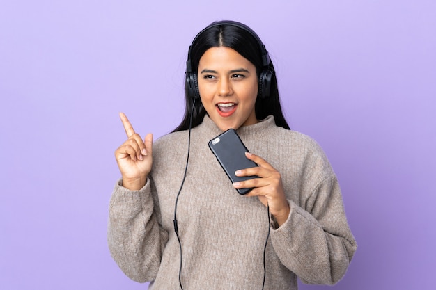 Junge lateinische Frau Frau lokalisiert auf lila hörende Musik mit einem Handy und Gesang