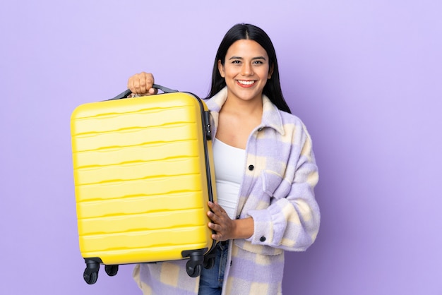 Junge lateinische Frau Frau lokalisiert auf lila im Urlaub mit Reisekoffer