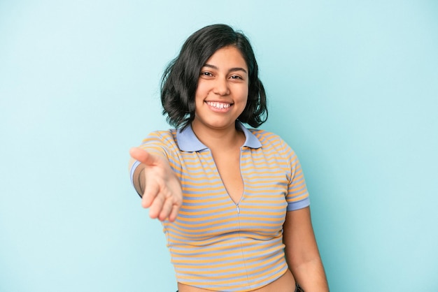 Junge lateinische Frau isoliert auf blauem Hintergrund, die Hand in die Kamera in Grußgeste ausdehnt.