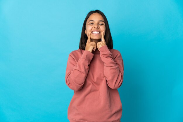 Junge lateinische Frau lokalisiert auf blauer Wand lächelnd mit einem glücklichen und angenehmen Ausdruck