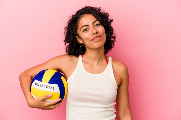 Junge lateinische Frau mit einem Volleyball auf rosa Hintergrund isoliert