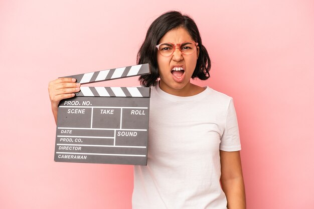 Junge lateinische Frau mit Klappe isoliert auf rosa Hintergrund schreien sehr wütend und aggressiv.