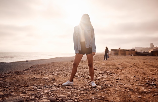 Junge lateinische Frau stellt während eines wunderschönen Sonnenuntergangs auf dem Sand spazieren Glückliche junge Frau mit Maske