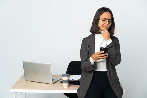 Junge lateinische Geschäftsfrau, die in einem Büro arbeitet, das auf weißem Denken isoliert wird und eine Nachricht sendet