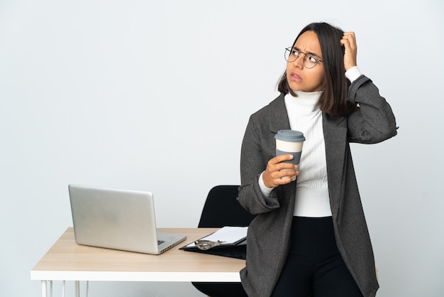 Junge lateinische Geschäftsfrau, die in einem Büro arbeitet, das auf weißem Hintergrund lokalisiert wird, der Zweifel beim Kratzen des Kopfes hat