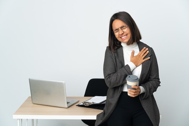 Junge lateinische geschäftsfrau, die in einem büro arbeitet, das auf weißer wand lokalisiert wird, die einen schmerz im herzen hat