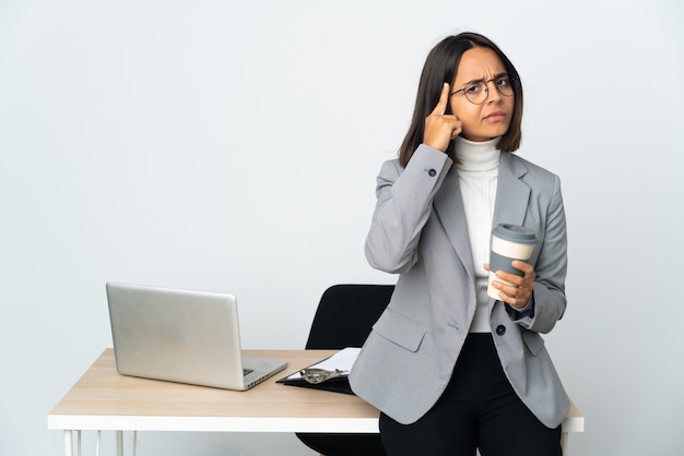 Junge lateinische Geschäftsfrau, die in einem Büro lokalisiert auf weißer Wand arbeitet, die eine Idee denkt