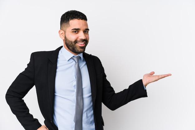 Junge lateinische Geschäftsfrau gegen eine weiße Wand, die eine leere Stelle auf einer Handfläche zeigt und eine andere Hand auf Taille hält.