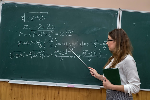 Junge Lehrer schreiben und erklären die mathematischen Formeln an einer Tafel. Ausbildung